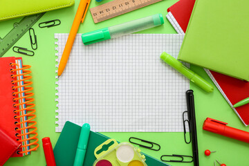 Frame made of different stationery with blank notebook on green background