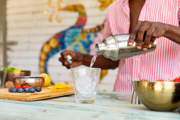 Midsection of biracial male bartender pouring cocktail from shaker at beach bar