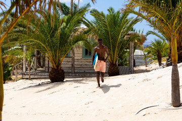 Biracial man carrying surfboard running on sunny beach