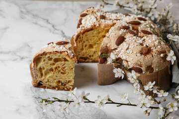 Delicious Italian Easter dove cake (traditional Colomba di Pasqua) and flowers on white marble table, closeup