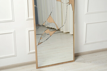 Broken mirror with many cracks near white wall indoors