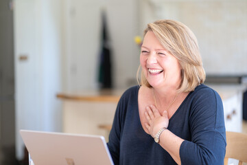 Laughing woman working at laptop in kitchen