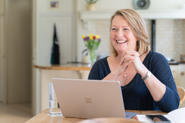 Smiling Woman using laptop working from home in kitchen