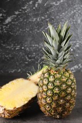 Whole and cut ripe pineapples on grey table near black wall