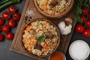 Delicious pilaf in bowls and products on black table, flat lay