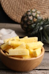 Pieces of tasty ripe pineapple in bowl on wooden table, closeup. Space for text