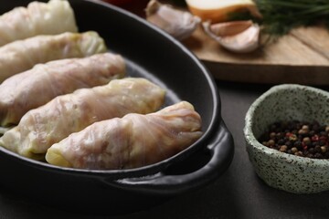 Uncooked stuffed cabbage rolls and spices on grey table, closeup