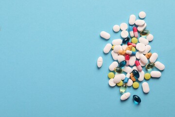 Pile of different pills on light blue background, flat lay. Space for text