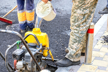 A worker fills the plastic tank of an old compact plate with water at a work site.