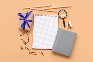 Gift box with magnifier and different stationery on orange background