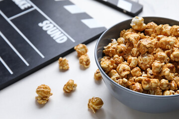 Bowl with tasty popcorn and clapperboard on white background