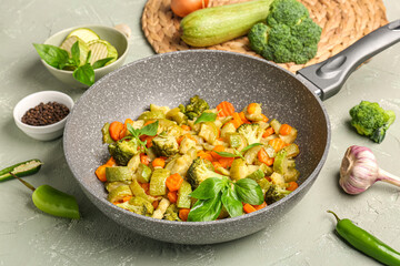 Frying pan with different vegetables on light background