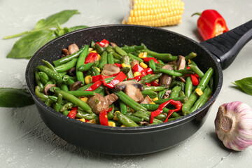 Frying pan with different vegetables on light background