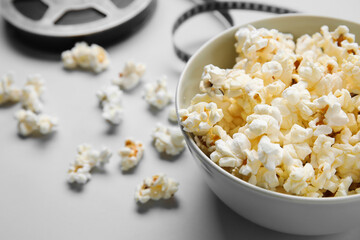 Bowl with tasty popcorn and film reel on grey background