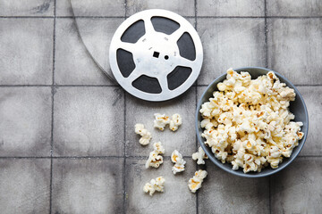 Bowl with tasty popcorn and film reel on grey tile background