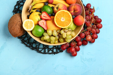 Bowl with different fresh fruits on blue background