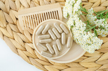 Small white bowl with food supplement capsules and yarrow flowers. Natural healthcare, herbal...
