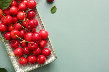Plate with sweet cherries on green background