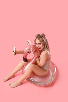 Young Woman In Swimsuit With Mobile Phone And Inflatable Ring On Pink Background