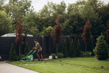 The man is working in the garden. Mowing grass with a lawn mower.