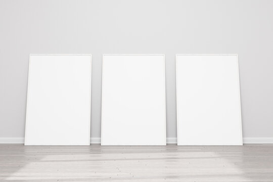 Models of paintings, posters, photographs. Three empty wooden frames for a photo or picture on the floor near a white wall. Design template for layout. 3D rendering.