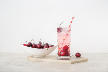 Glass of tasty cherry lemonade and bowl with berries on white background