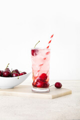 Glass of tasty cherry lemonade and bowl with berries on white background