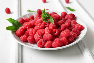 Plate with fresh raspberries and mint on white background