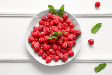 Plate with fresh raspberries and mint on white background
