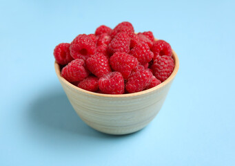 Bowl with fresh raspberries on blue background