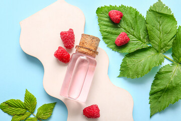 Decorative podium with bottle of cosmetic raspberry oil on blue background