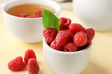 Bowl with fresh raspberries and cup of tea on yellow table
