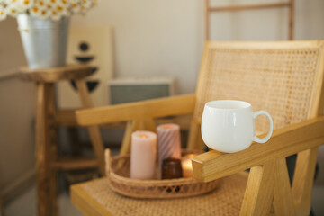 Fototapeta na wymiar White mug with green tea and bouquet of chamomiles on wooden table in cozy living room.