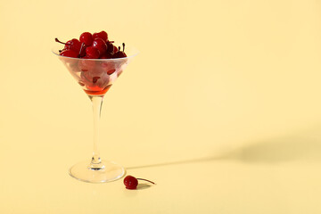 Glass of tasty maraschino cherries on yellow background