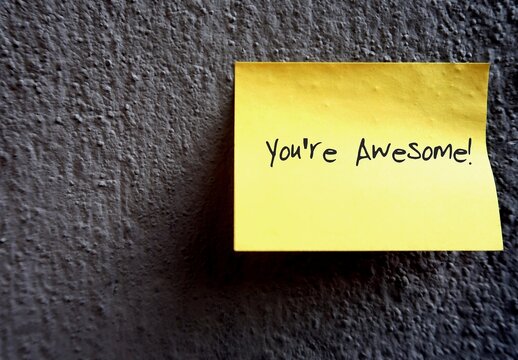 Yellow note on copy space wall background with text written YOU'RE AWESOME!, to express feeling of extremely impressive, inspiring great admiration, to say something is great