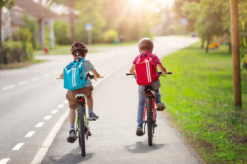 Two boys with backpacks on bicycles going to school.