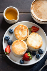 Syrniki, cottage cheese fritters with fresh berries, syrup and cup of coffee