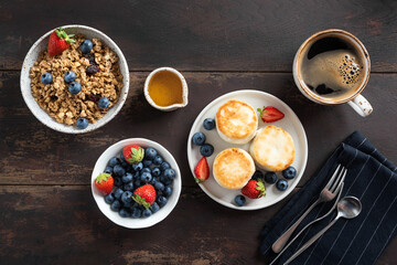 Breakfast table with morning coffee, granola bowl and cottage cheese fritters served with fresh summer berries and honey. Top view, wooden table background