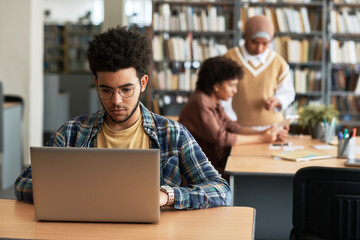 Adult student sitting in library and learning foreign language online using his laptop