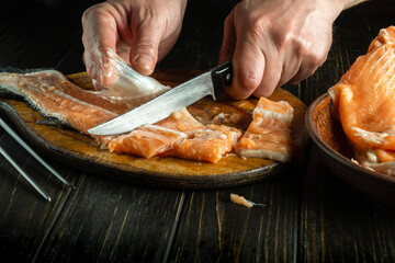 Butcher hands with a knife butcher a fish carcass on a cutting board. The concept of cooking a fish dish