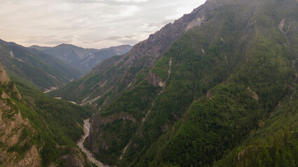 Naklejka premium Aerial view of a high valley of the rocky mountain range, on which snow lies in places, near to the fast mountain river at summer cloud morning, orange color