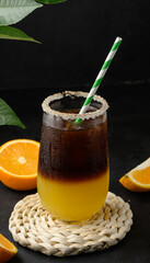 Iced coffee with orange juice in a transparent glass, refreshing bumble coffee on the table, black background