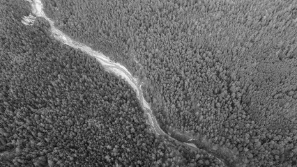 Aerial view of the high waterfall and fast mountain river in valley of the rocky mountain ranges, on which snow lies in places at summer cloud morning, gray