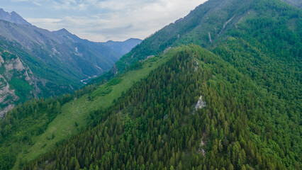 Aerial view of a high valley of the rocky mountain range, on which snow lies in places, near to the fast mountain river at summer cloud morning, green color 