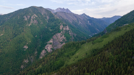 Naklejka premium Aerial view of a high valley of the rocky mountain range, on which snow lies in places, near to the fast mountain river at summer cloud morning, orange color of the photo
