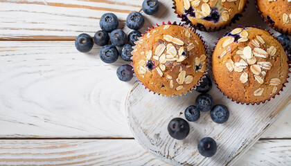 Fototapeta na wymiar Freshly baked blueberry muffins with almond, oats and icing sugar topping on a rustic white wooden table with berries, brown sugar. Top view
