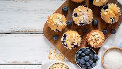 Fotobehang Freshly baked blueberry muffins with almond, oats and icing sugar topping on a rustic white wooden table with berries, brown sugar. Top view © Uuganbayar