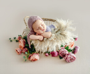 Newborn baby girl sleeping on fur and peony flowers. Cute infant child kid napping in basket studio portrait