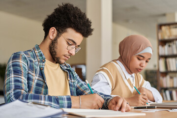Multiethnic students writing foreign language exam at table in class