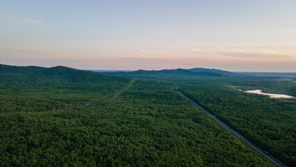 Fototapeta premium Aerial view of the Mountain range and tall forest near to the river at summer cloud evening with incredible horizon, orange color